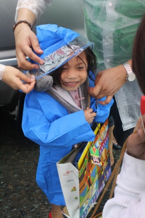 A child excitedly wore her raincoat as volunteers assisted her.